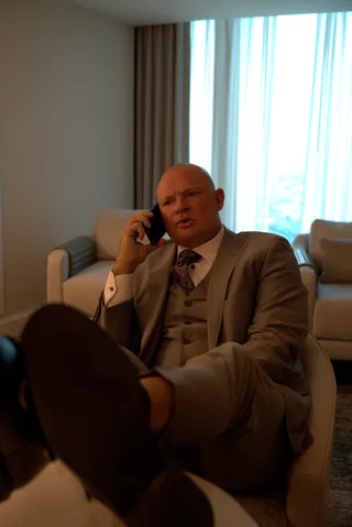 Shawn sits back in an armchair with feet resting up while talking on the phone in a luxurious room.
