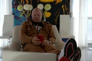 Shawn sits back in a white armchair looking down at a red smartphone.