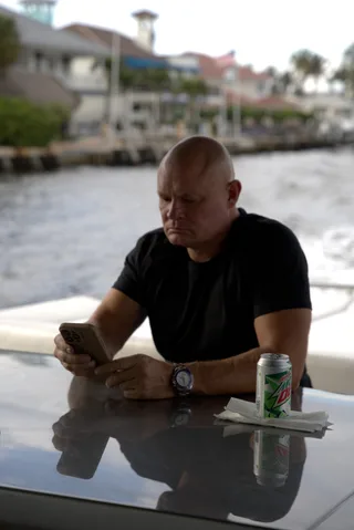 Shawn sits at a table on a boat looking down at a phone.