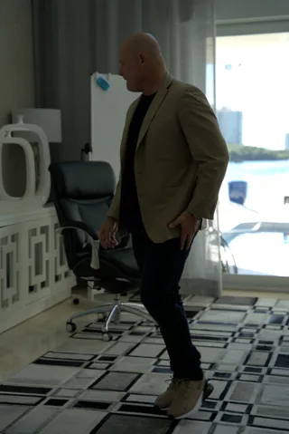 Shawn in a blazer and jeans walks across a room past an office chair.