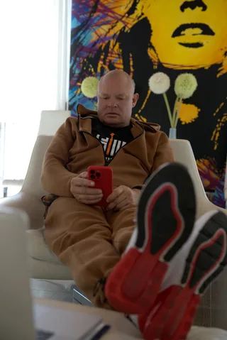 Shawn looks at a smartphone while relaxing in a chair at home with feet up.