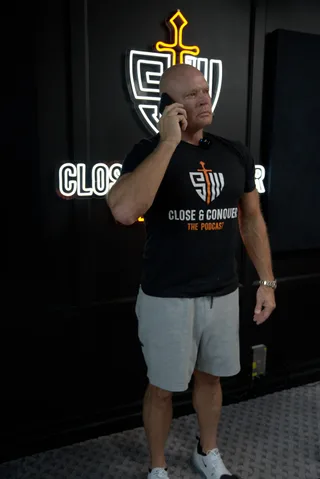 Shawn holds a phone to his ear while standing in front of a podcast wall backdrop.