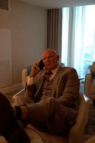 Shawn sits in an armchair wearing a suit while talking on a mobile phone.