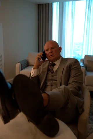 Shawn talks on a mobile phone while resting feet on a table inside a room.