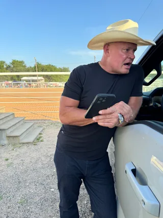 Shawn looks at a phone while leaning against a truck outdoors.