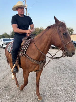 Shawn rides a horse on a gravel path outdoors.