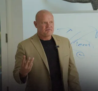 Shawn is speaking and gesturing near a whiteboard in an office.