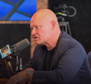 Shawn speaks into a microphone at a desk in a studio.