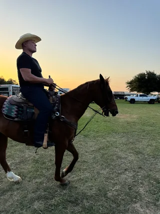Shawn rides a horse through a field during sunset.