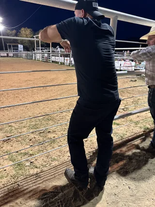 Shawn watches an event from behind a metal fence at a rodeo arena.