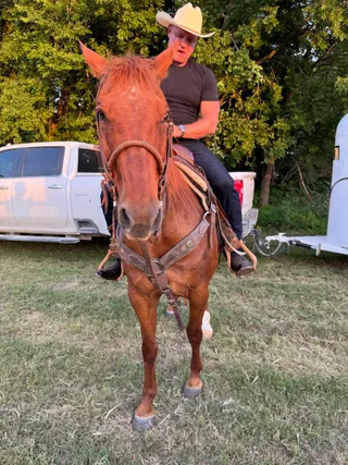 Shawn wears a cowboy hat while riding a horse outdoors near a truck.