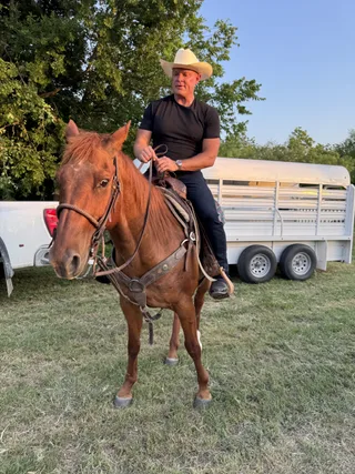 Shawn rides a brown horse outdoors near a truck and trailer.