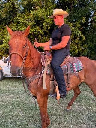 Shawn sits on a horse outdoors during golden hour.