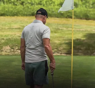 Shawn stands on a golf course putting green.
