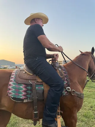 Shawn rides a horse outdoors at sunset.