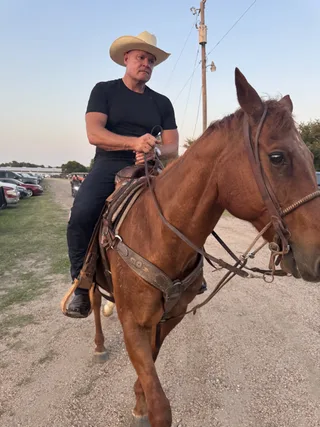 Shawn rides a horse on a dirt path outdoors.