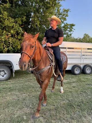 Shawn rides a horse outdoors near a truck and trailer.