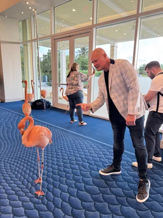 Shawn points at a flamingo inside a hotel lobby with large windows and blue patterned carpet.