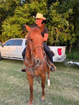 Shawn sits on a horse outdoors with a truck in the background.