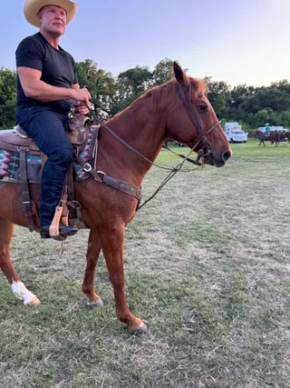Shawn rides a brown horse in an outdoor field.