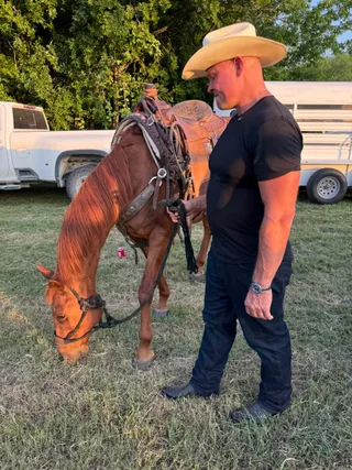 Shawn stands next to a horse grazing in an outdoor field.
