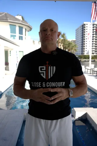 Shawn stands by a swimming pool outdoors in front of a house.