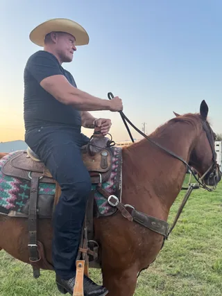 Shawn rides a brown horse in an outdoor pasture.