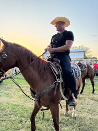 Shawn wears a cowboy hat while riding a horse outdoors at sunset.