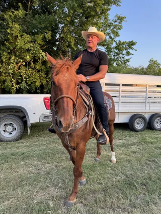 Shawn rides a horse outdoors near a truck and trailer.