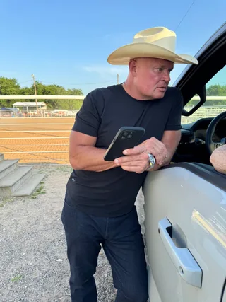 Shawn looking at a phone while leaning against a truck outdoors.
