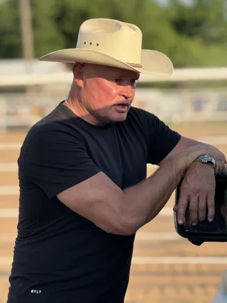 Shawn wearing a cowboy hat leans against a vehicle outdoors.
