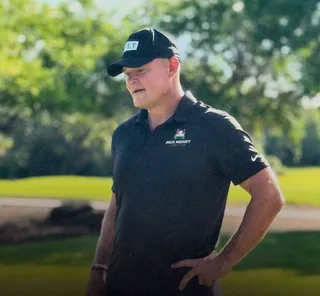 Shawn stands on a golf course outdoors.
