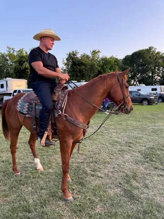 Shawn sits on a horse in an outdoor field during evening.