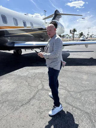 Shawn stands on an airport tarmac next to a private jet while holding a smartphone.