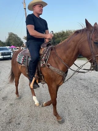 Shawn rides a brown horse outdoors.