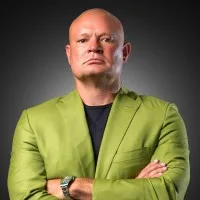 Shawn wearing a green jacket stands with crossed arms against a dark background.