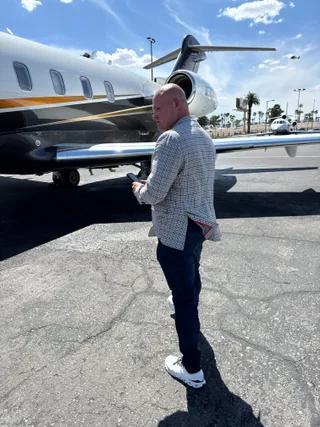 Shawn stands by a private jet on an airport tarmac while looking at a phone.